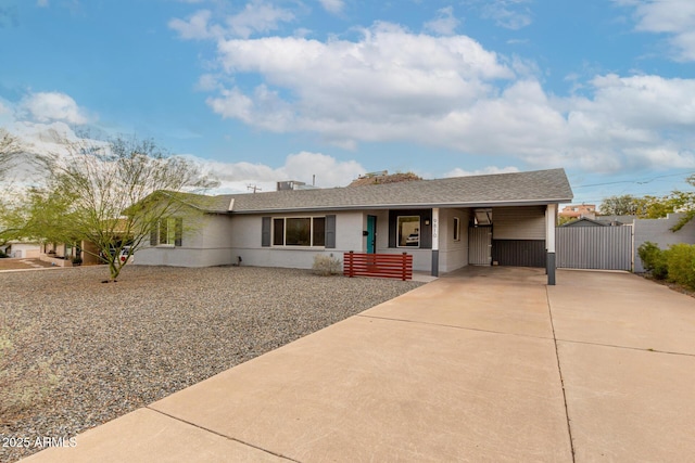 ranch-style house with concrete driveway, a gate, a carport, and a shingled roof