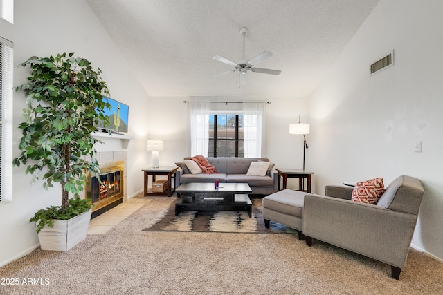 carpeted living room with visible vents, lofted ceiling, ceiling fan, a textured ceiling, and a tile fireplace