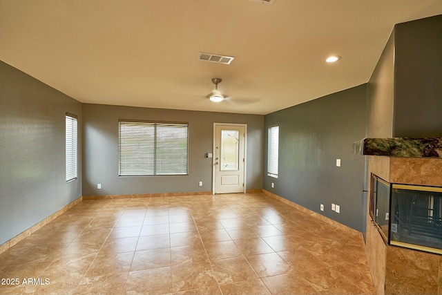 interior space with visible vents, light tile patterned flooring, ceiling fan, a tile fireplace, and baseboards