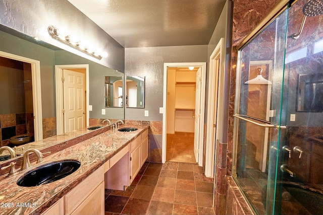 full bathroom with a spacious closet, stone finish floor, a sink, and a shower stall