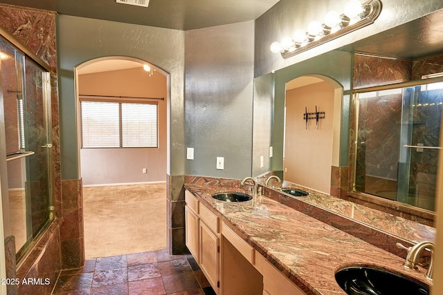 bathroom featuring visible vents, double vanity, a sink, and stone tile flooring