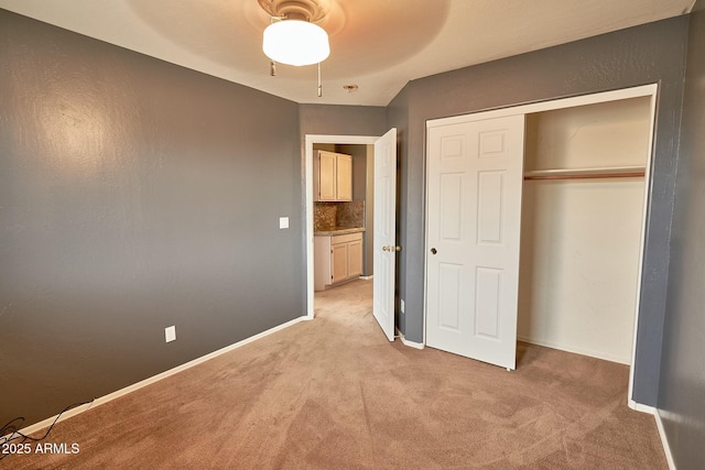 unfurnished bedroom with a closet, light colored carpet, ceiling fan, and baseboards