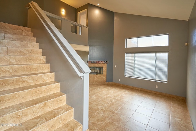 stairs with high vaulted ceiling, tile patterned flooring, and a premium fireplace