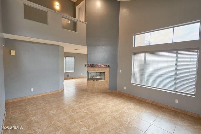 unfurnished living room featuring a towering ceiling, light tile patterned floors, a fireplace, and baseboards