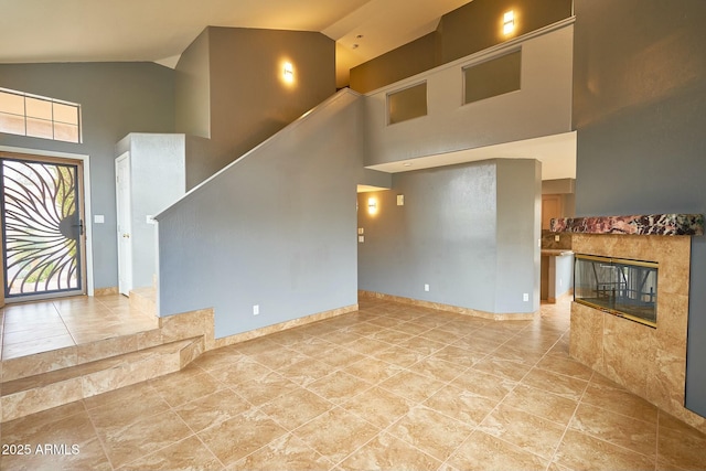 unfurnished living room with stairway, baseboards, a fireplace, and high vaulted ceiling