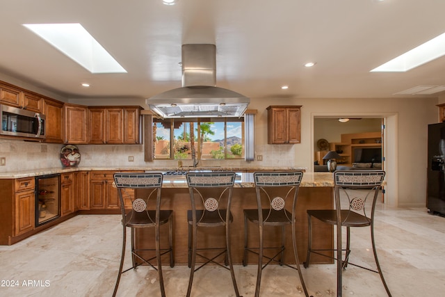 kitchen featuring a skylight, brown cabinetry, a center island, stainless steel microwave, and a kitchen bar