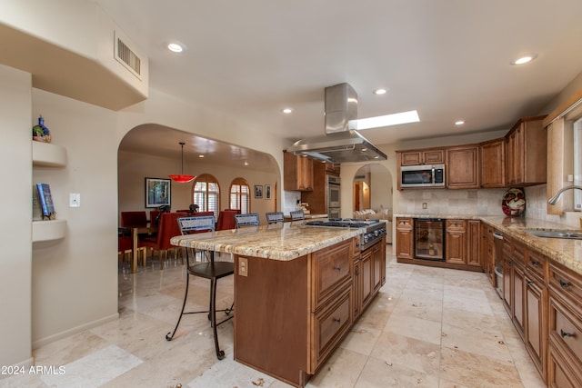 kitchen with island exhaust hood, a breakfast bar area, appliances with stainless steel finishes, brown cabinetry, and a sink