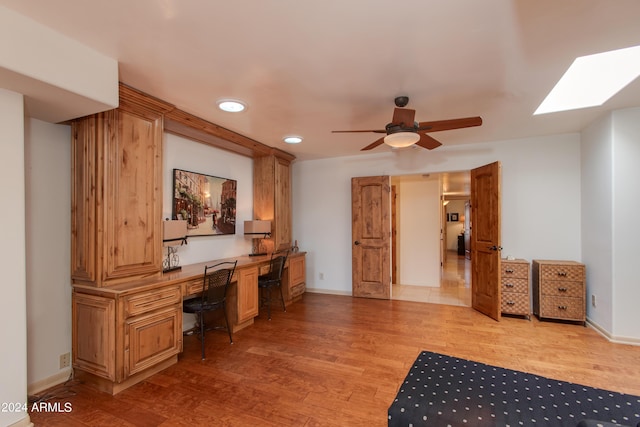 home office with a ceiling fan, light wood-type flooring, baseboards, and a skylight