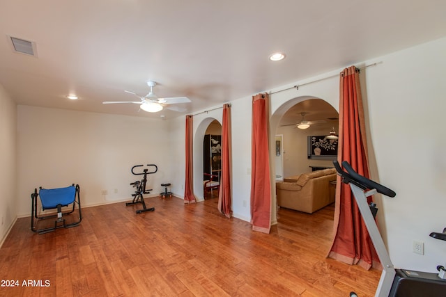 exercise room featuring arched walkways, light wood finished floors, a fireplace, and a ceiling fan