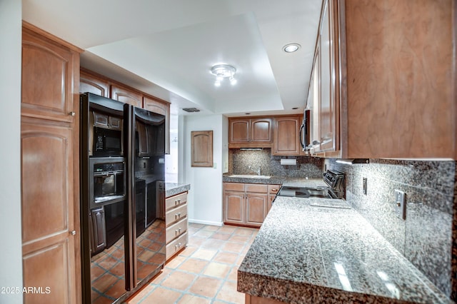 kitchen featuring backsplash, electric range oven, brown cabinets, a raised ceiling, and a sink