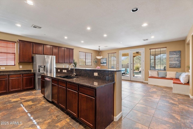 kitchen featuring sink, hanging light fixtures, dark stone counters, a center island with sink, and appliances with stainless steel finishes