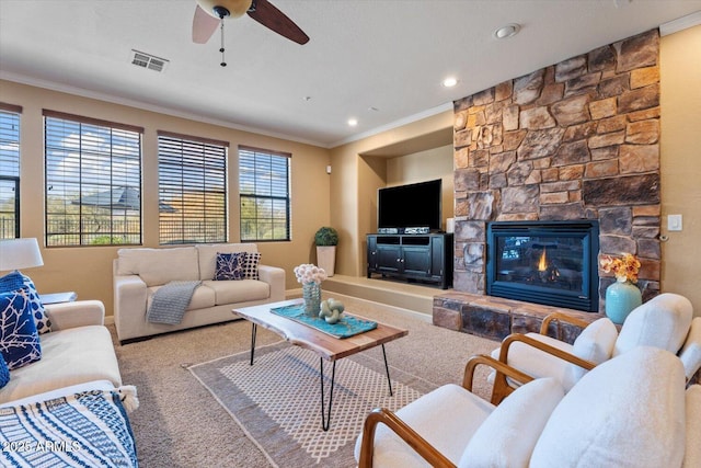 carpeted living room with a stone fireplace, ceiling fan, and crown molding