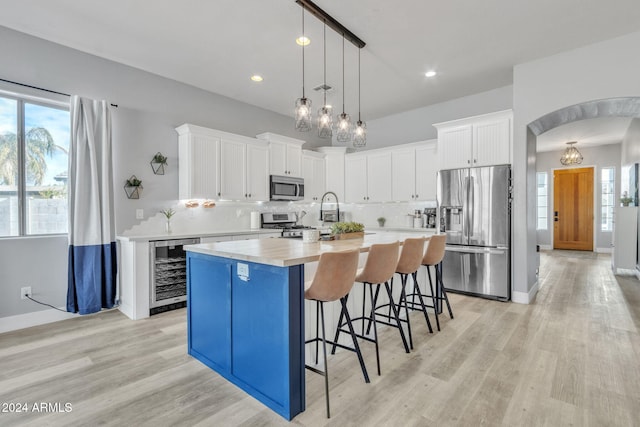 kitchen with tasteful backsplash, stainless steel appliances, beverage cooler, white cabinets, and an island with sink