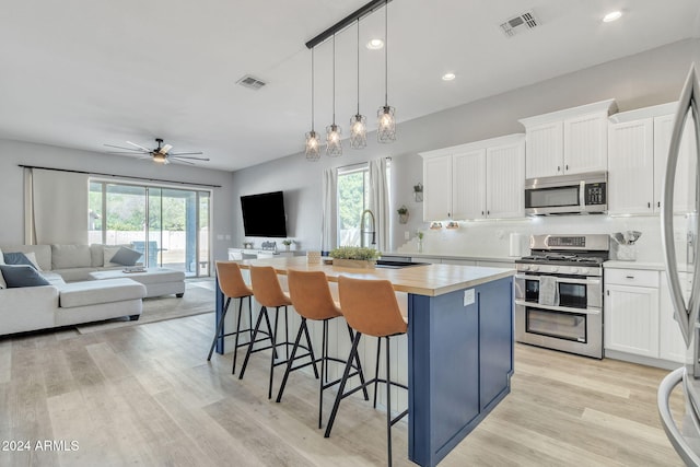 kitchen featuring a kitchen island with sink, hanging light fixtures, ceiling fan, appliances with stainless steel finishes, and white cabinetry