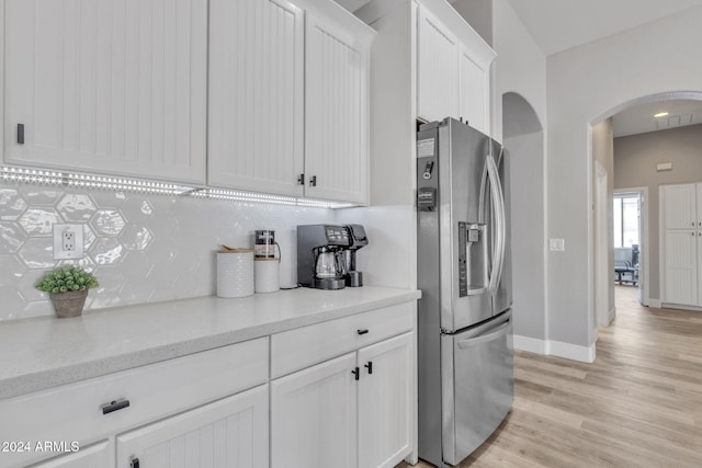 kitchen featuring light stone countertops, stainless steel refrigerator with ice dispenser, backsplash, light wood-type flooring, and white cabinets