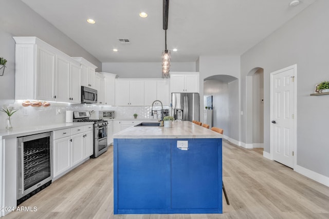 kitchen with sink, beverage cooler, decorative light fixtures, a center island with sink, and appliances with stainless steel finishes