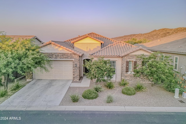 mediterranean / spanish house with an attached garage, stone siding, driveway, and a tiled roof