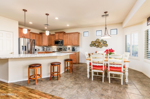 kitchen with visible vents, brown cabinets, stainless steel appliances, tasteful backsplash, and a breakfast bar area