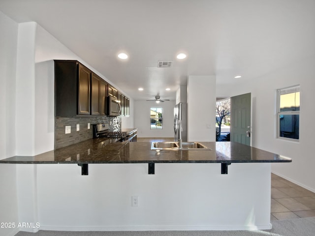 kitchen featuring visible vents, appliances with stainless steel finishes, a sink, dark brown cabinets, and a peninsula