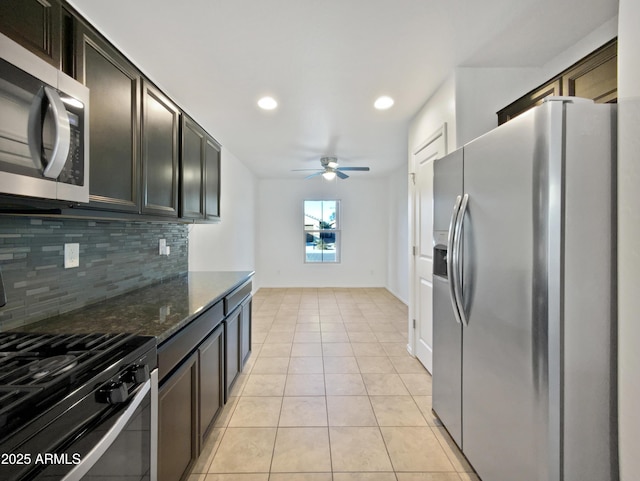 kitchen featuring light tile patterned floors, a ceiling fan, appliances with stainless steel finishes, tasteful backsplash, and dark stone countertops