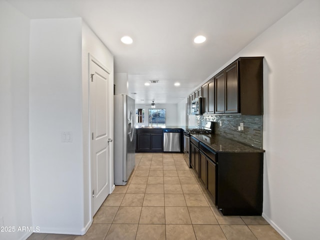 kitchen featuring light tile patterned flooring, dark brown cabinets, appliances with stainless steel finishes, decorative backsplash, and dark stone counters