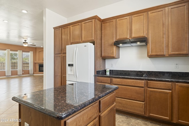 kitchen with ceiling fan, white fridge with ice dispenser, a fireplace, a kitchen island, and black stovetop