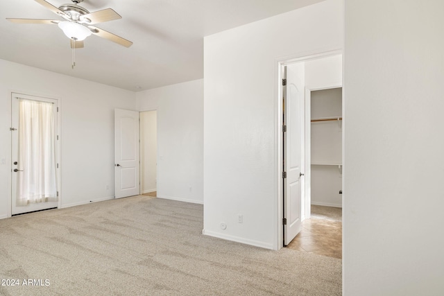 unfurnished bedroom with a closet, light colored carpet, a spacious closet, and ceiling fan