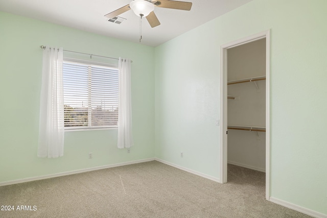 unfurnished bedroom featuring a closet, a spacious closet, ceiling fan, and light colored carpet