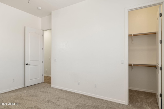 unfurnished bedroom featuring a walk in closet, light colored carpet, and a closet