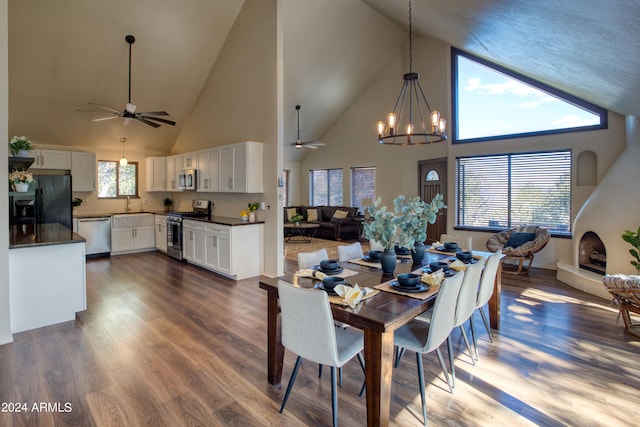 dining area with sink, ceiling fan with notable chandelier, dark wood-type flooring, and high vaulted ceiling