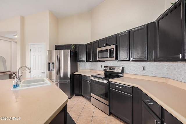 kitchen featuring sink, light tile patterned floors, a towering ceiling, stainless steel appliances, and decorative backsplash