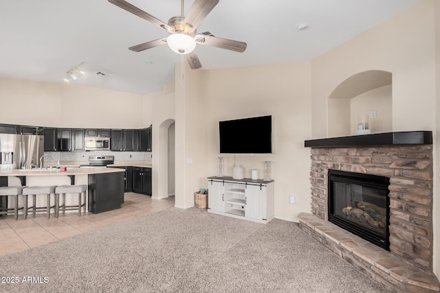 tiled living room with ceiling fan, a fireplace, and a towering ceiling