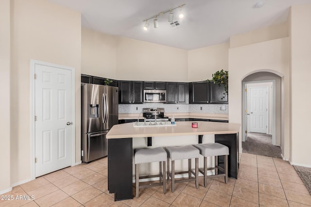 kitchen with appliances with stainless steel finishes, a breakfast bar, a kitchen island with sink, and a towering ceiling