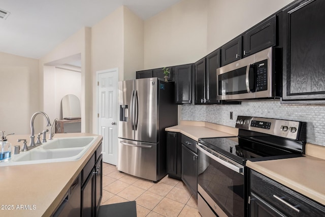 kitchen with vaulted ceiling, appliances with stainless steel finishes, sink, backsplash, and light tile patterned floors