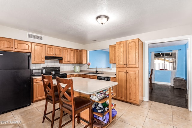 kitchen featuring a textured ceiling, black appliances, sink, and light tile patterned floors