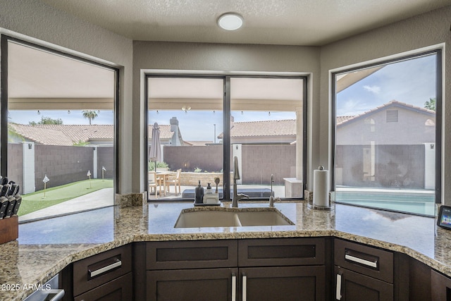 1461 W Tara Dr, Gilbert, AZ 85233 - kitchen featuring a sink, plenty of natural light, dark brown cabinetry, light stone countertops, and a textured wall