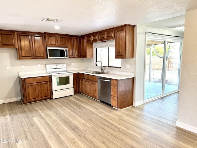 kitchen featuring stainless steel appliances, sink, a textured ceiling, and light wood-type flooring