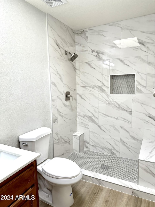 bathroom featuring vanity, tiled shower, hardwood / wood-style floors, and toilet