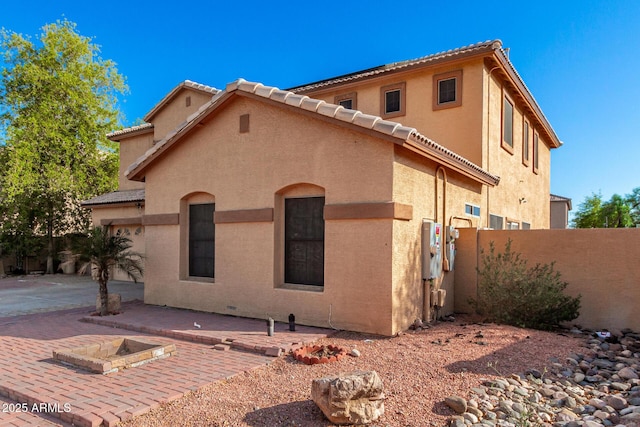 rear view of house featuring a tiled roof, fence, a patio, and stucco siding
