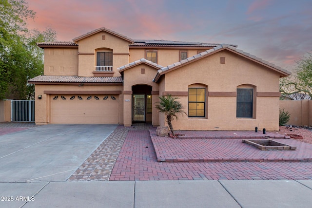 mediterranean / spanish-style home featuring stucco siding, driveway, a tile roof, fence, and roof mounted solar panels