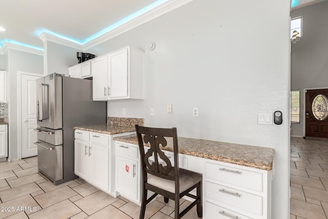 kitchen featuring freestanding refrigerator, light stone countertops, ornamental molding, white cabinets, and light tile patterned flooring