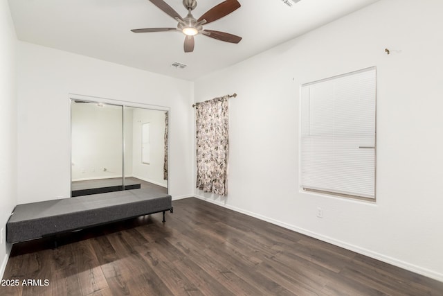 unfurnished bedroom featuring a closet, a ceiling fan, visible vents, wood finished floors, and baseboards