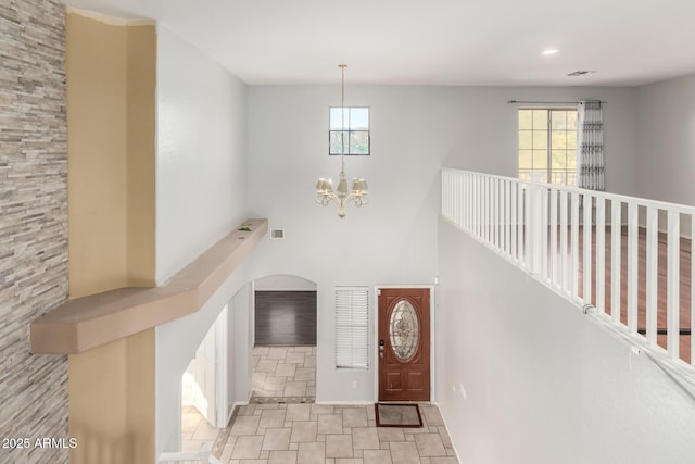 foyer with arched walkways, a notable chandelier, a high ceiling, and visible vents