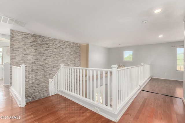 hallway with wood finished floors, visible vents, an upstairs landing, and plenty of natural light