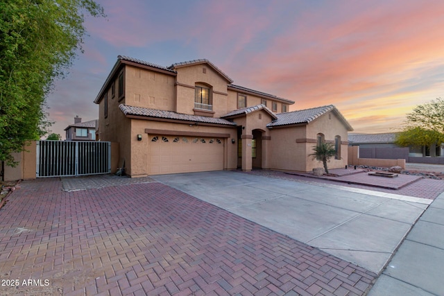 mediterranean / spanish-style home with stucco siding, driveway, an attached garage, a tile roof, and a gate