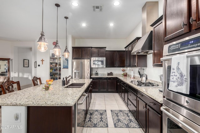 kitchen with decorative light fixtures, light tile patterned floors, stainless steel appliances, a center island with sink, and wall chimney exhaust hood