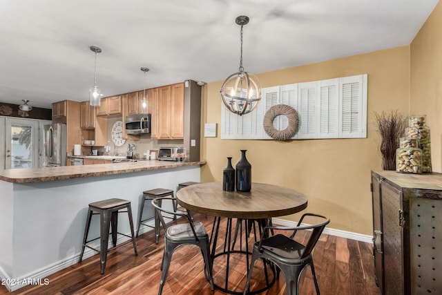 kitchen with hanging light fixtures, stainless steel appliances, a kitchen breakfast bar, kitchen peninsula, and hardwood / wood-style flooring