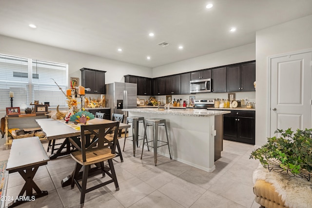 kitchen with appliances with stainless steel finishes, a kitchen breakfast bar, sink, light tile patterned floors, and an island with sink