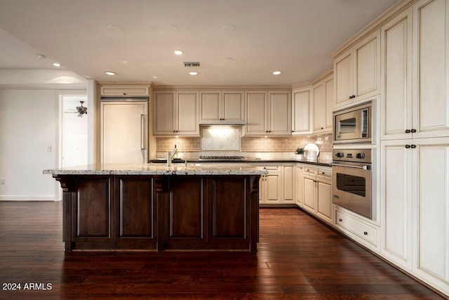 kitchen featuring tasteful backsplash, dark stone counters, dark wood-type flooring, cream cabinets, and built in appliances