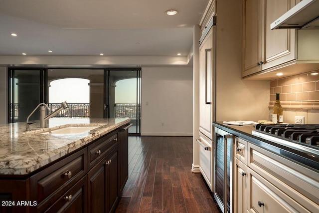 kitchen with light stone countertops, sink, beverage cooler, dark hardwood / wood-style flooring, and dark brown cabinets